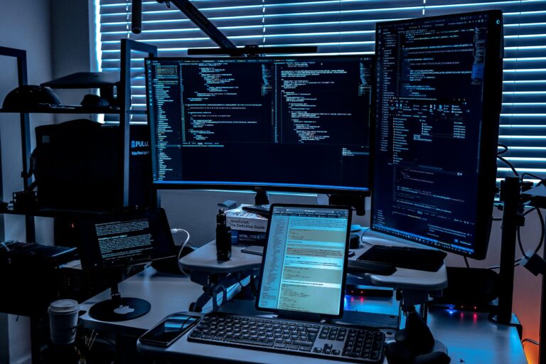 Dark developer workstation with multiple monitors showing code in blue light — the SMB AI coding agent setup