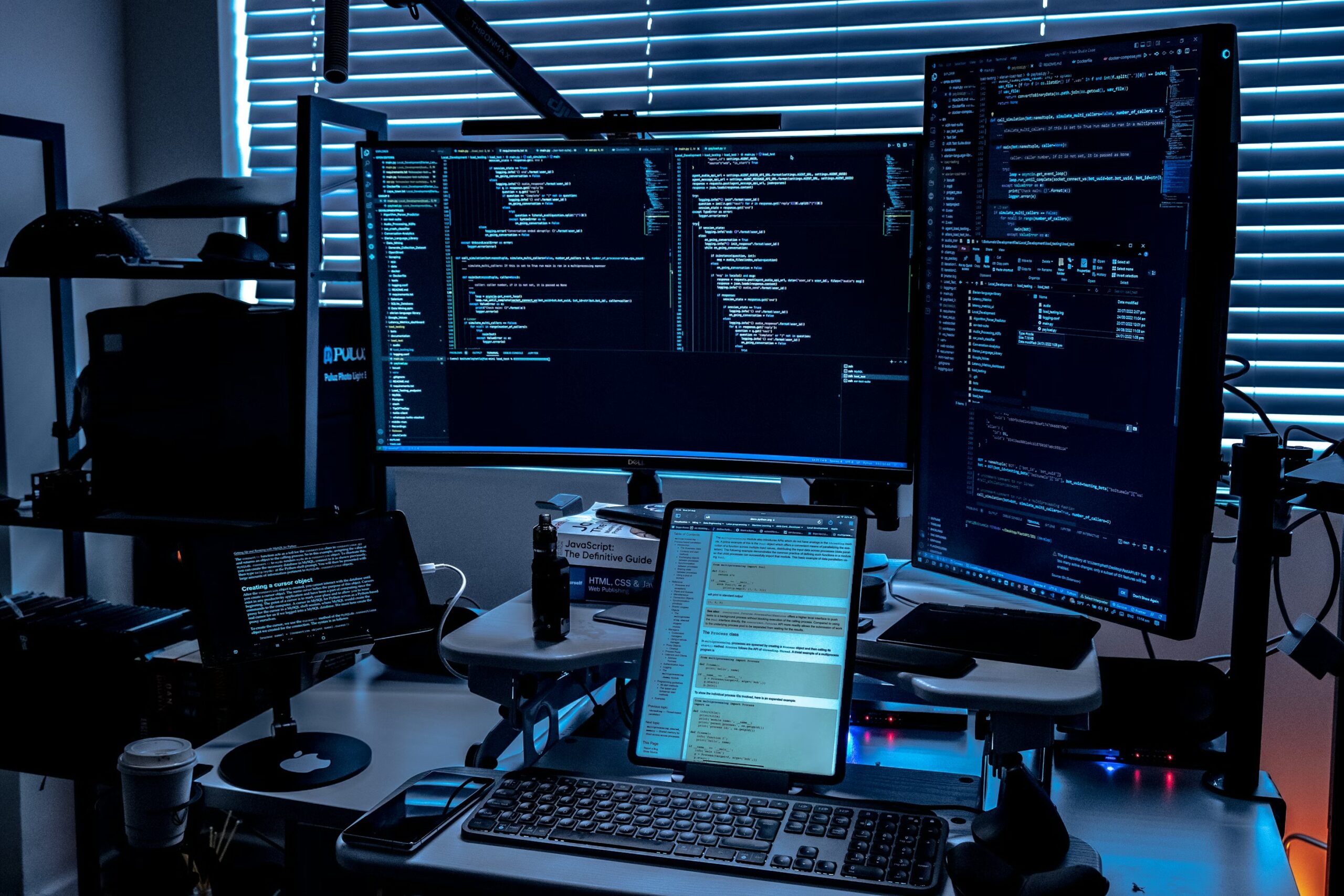 Dark developer workstation with multiple monitors showing code in blue light — the SMB AI coding agent setup